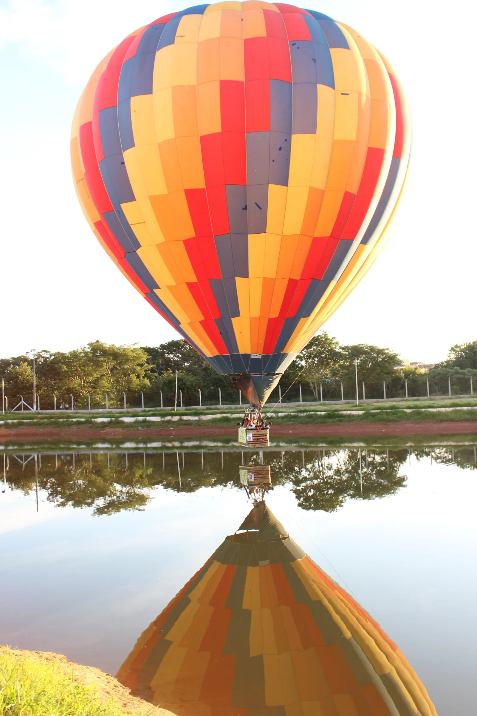 Balão de ar quente colorido voando baixo sobre um lago, refletido na água