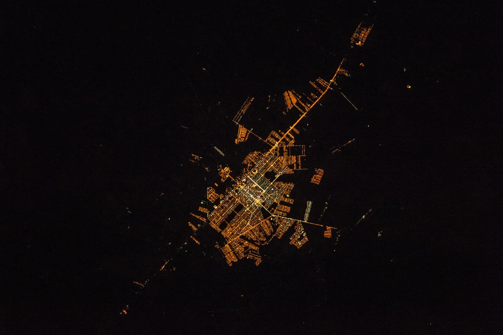 A malha urbana de Sinop iluminada à noite, vista do espaço, cortada pela rodovia