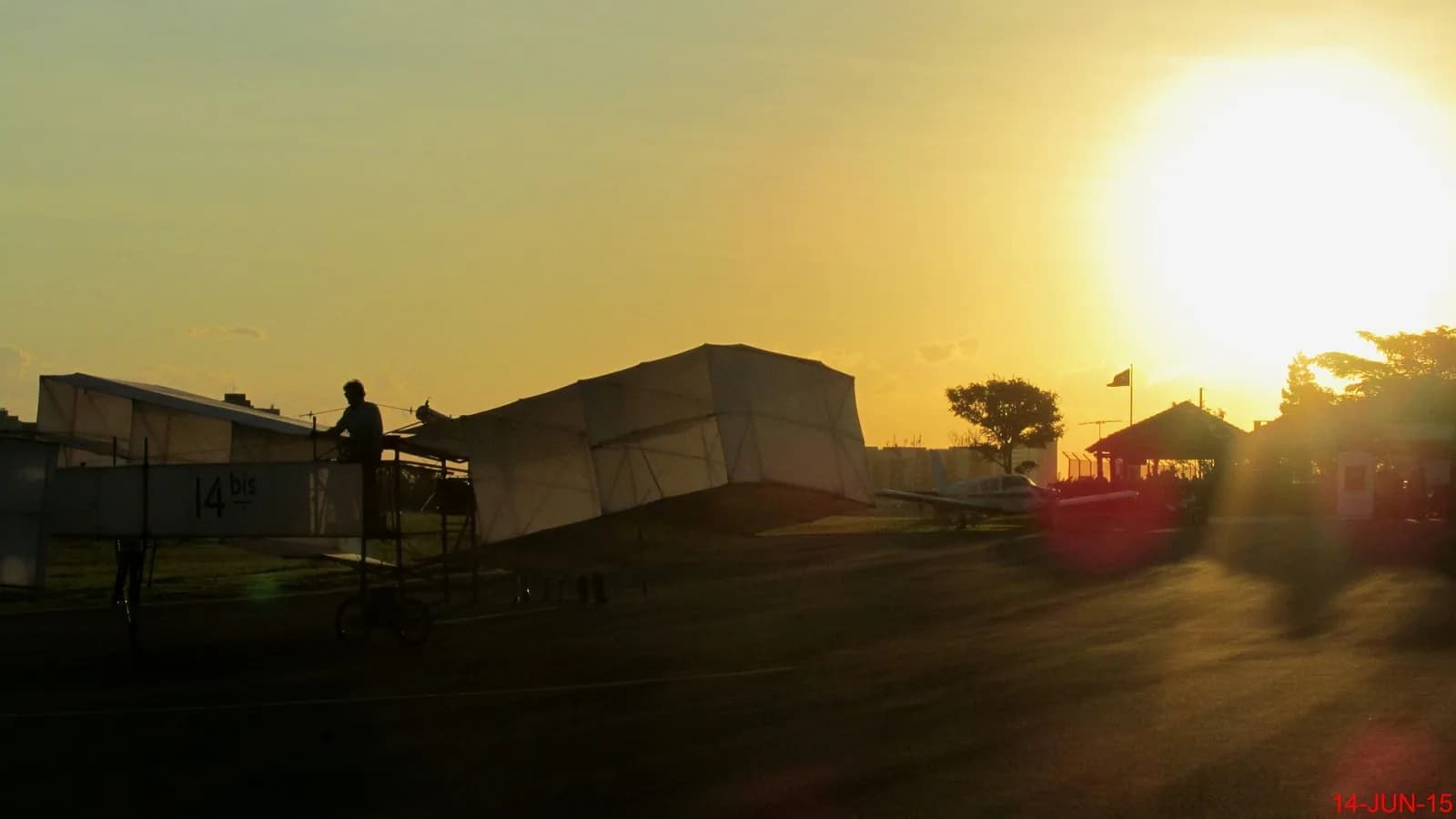 Silhueta da réplica do 14-Bis, com a inscrição 14 bis, no pátio de um aeródromo ao pôr do sol