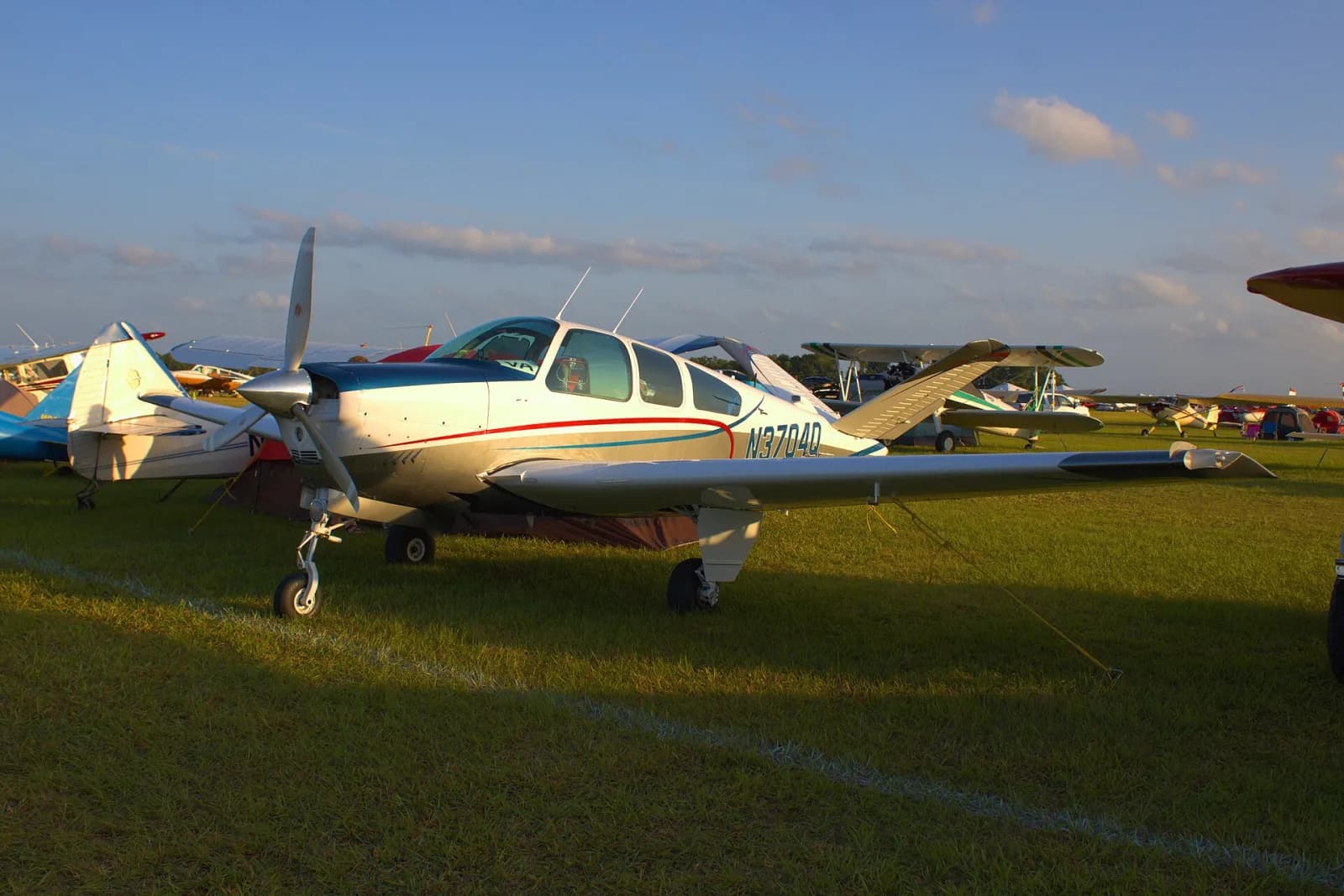 Beechcraft V35 Bonanza de cauda em V estacionado na grama ao entardecer, com outros aviões ao fundo