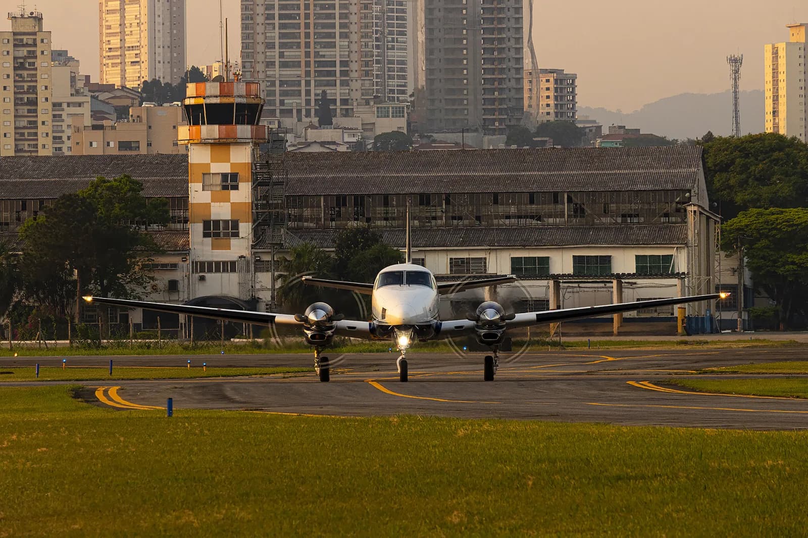 Beechcraft King Air taxiando no Campo de Marte, com a torre de controle e os hangares do PAMA-SP ao fundo