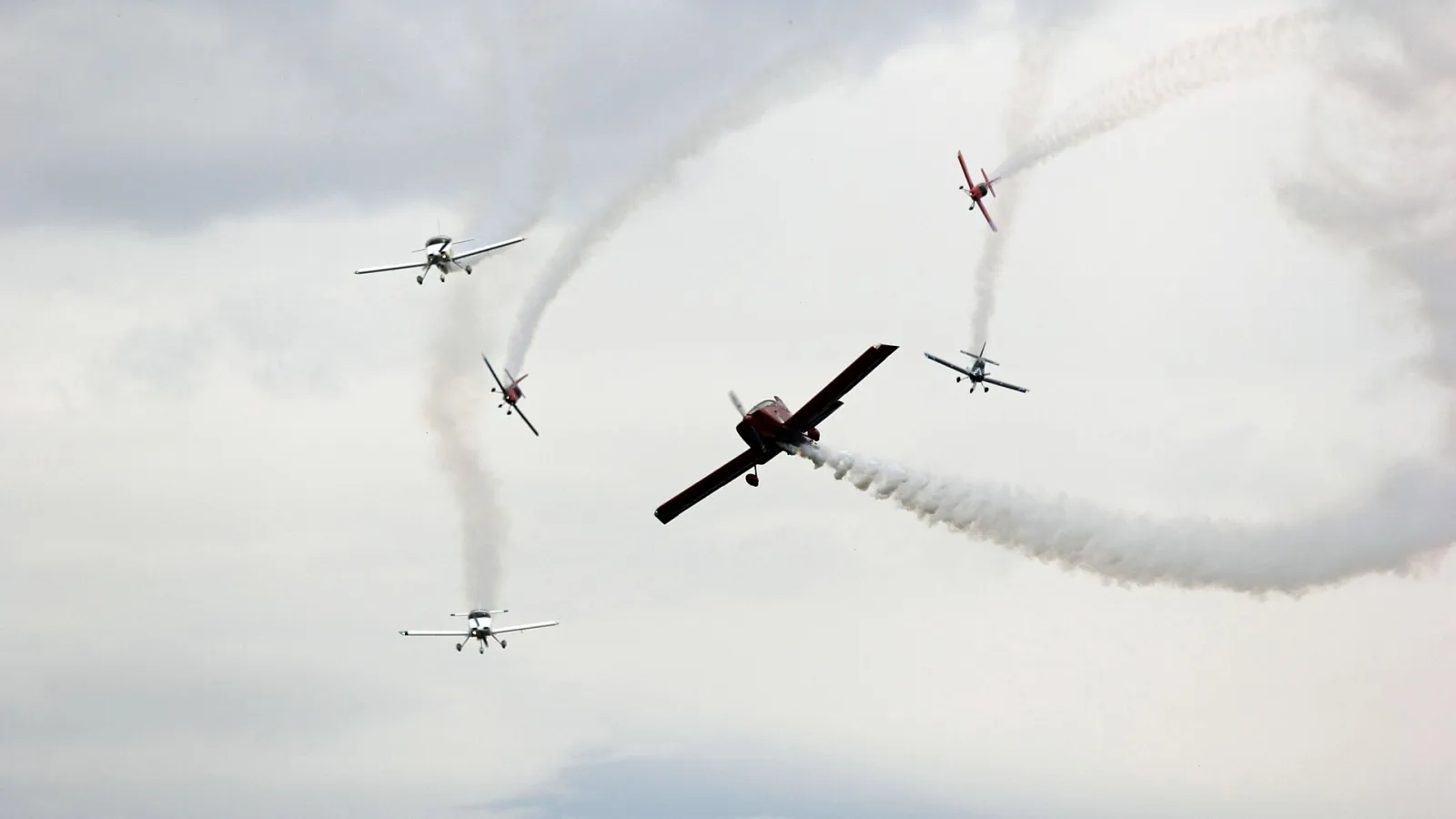 Aviões da Esquadrilha CEU se separando em direções diferentes durante uma manobra, deixando rastros de fumaça em curva