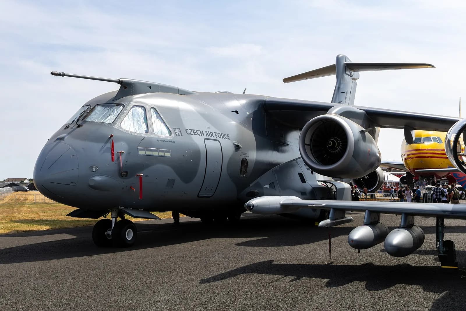 Cargueiro Embraer C-390 cinza da Força Aérea Tcheca estacionado no pátio de exposição, com o público ao fundo