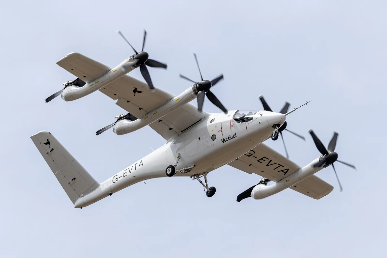 Aeronave elétrica de decolagem vertical branca, matrícula G-EVTA, com oito hélices nas asas, vista de baixo em voo