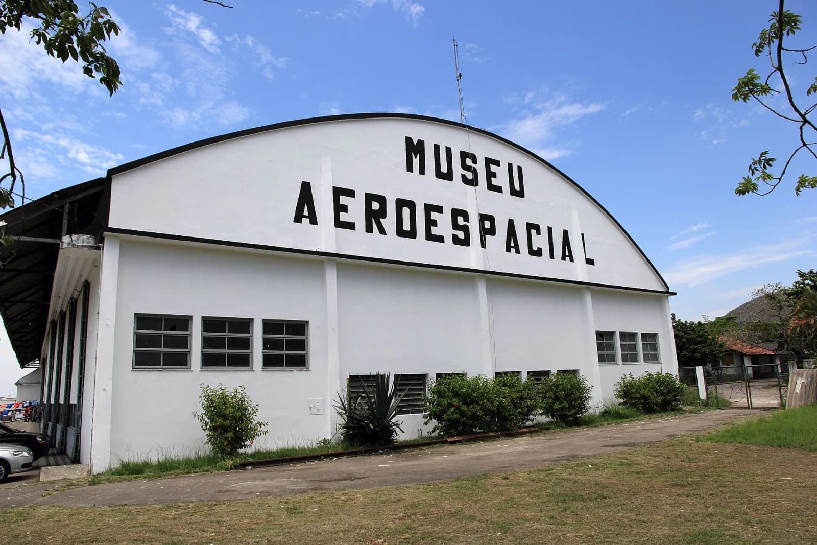 Hangar branco com fachada em arco e o letreiro Museu Aeroespacial, sob céu azul