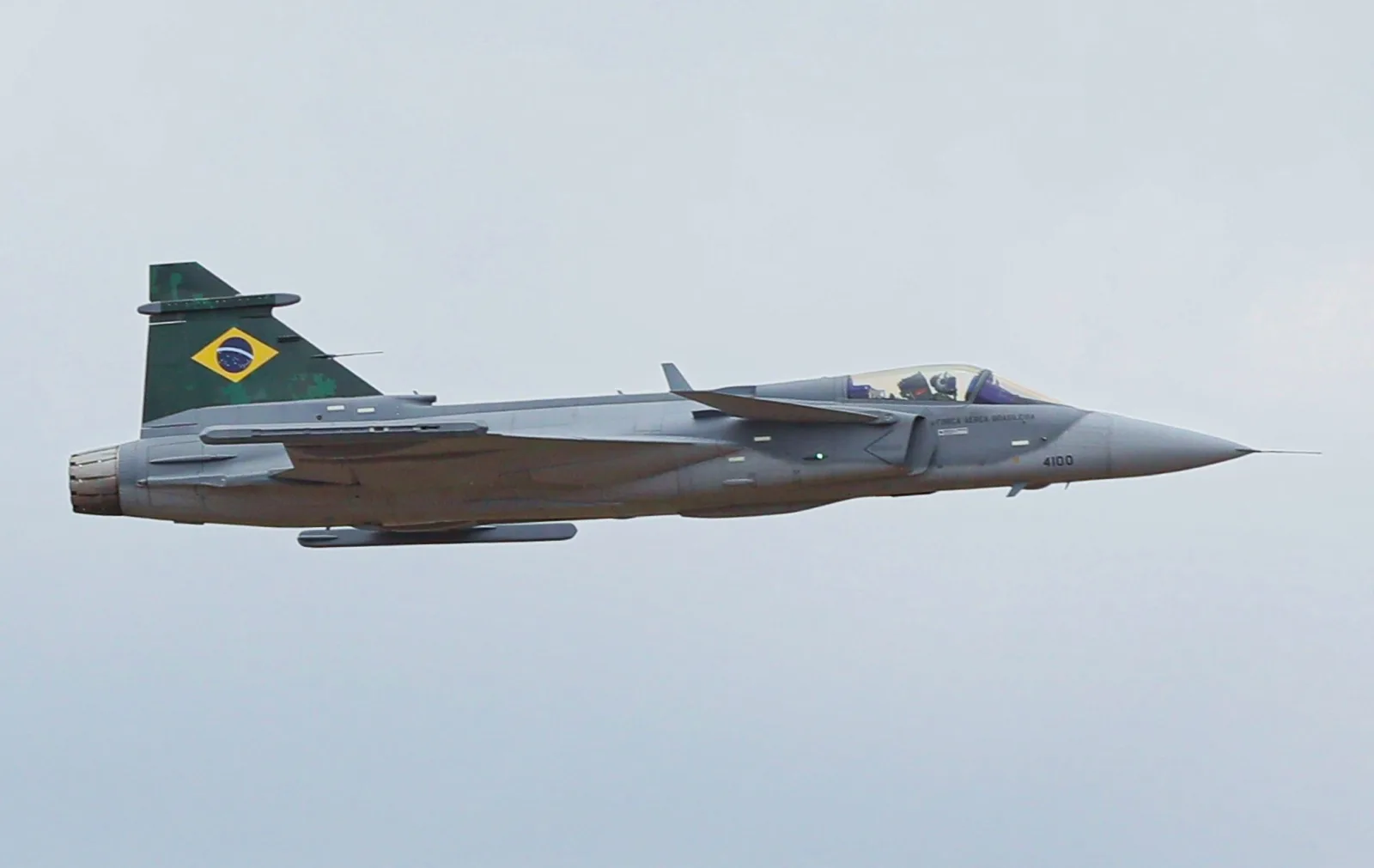 Caça F-39E Gripen com a bandeira do Brasil na deriva, em voo nivelado contra o céu nublado