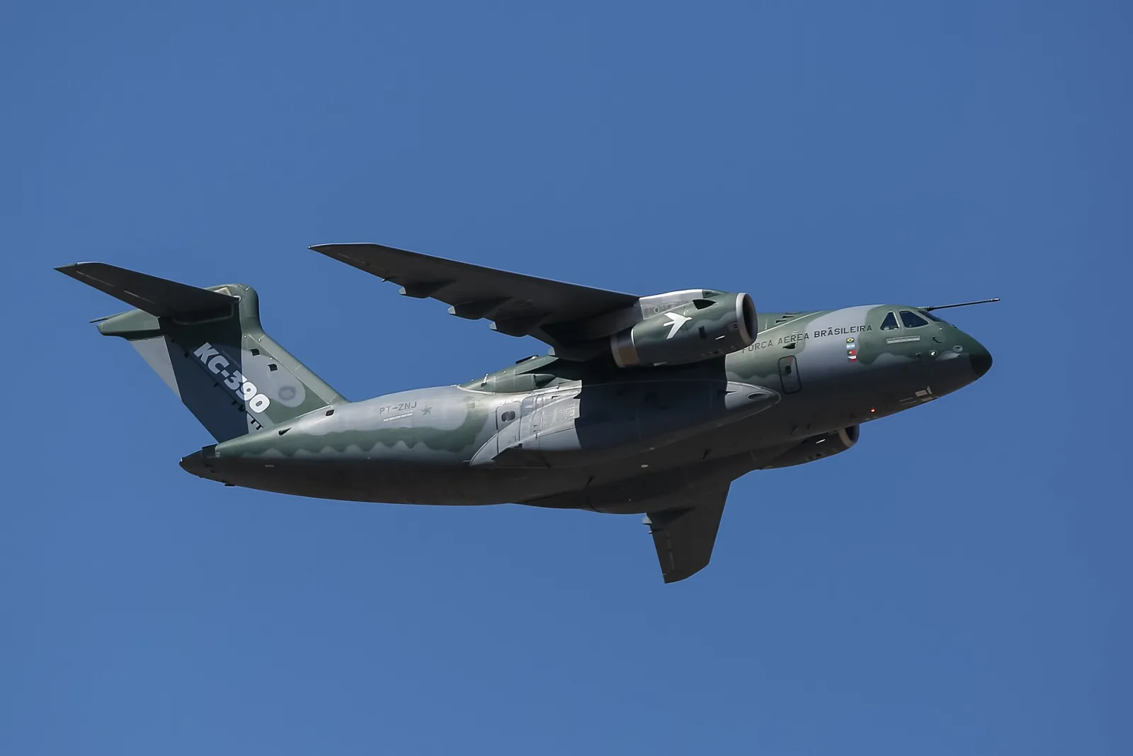 Cargueiro KC-390 com pintura camuflada verde e cinza e a inscrição Força Aérea Brasileira, em voo contra o céu azul