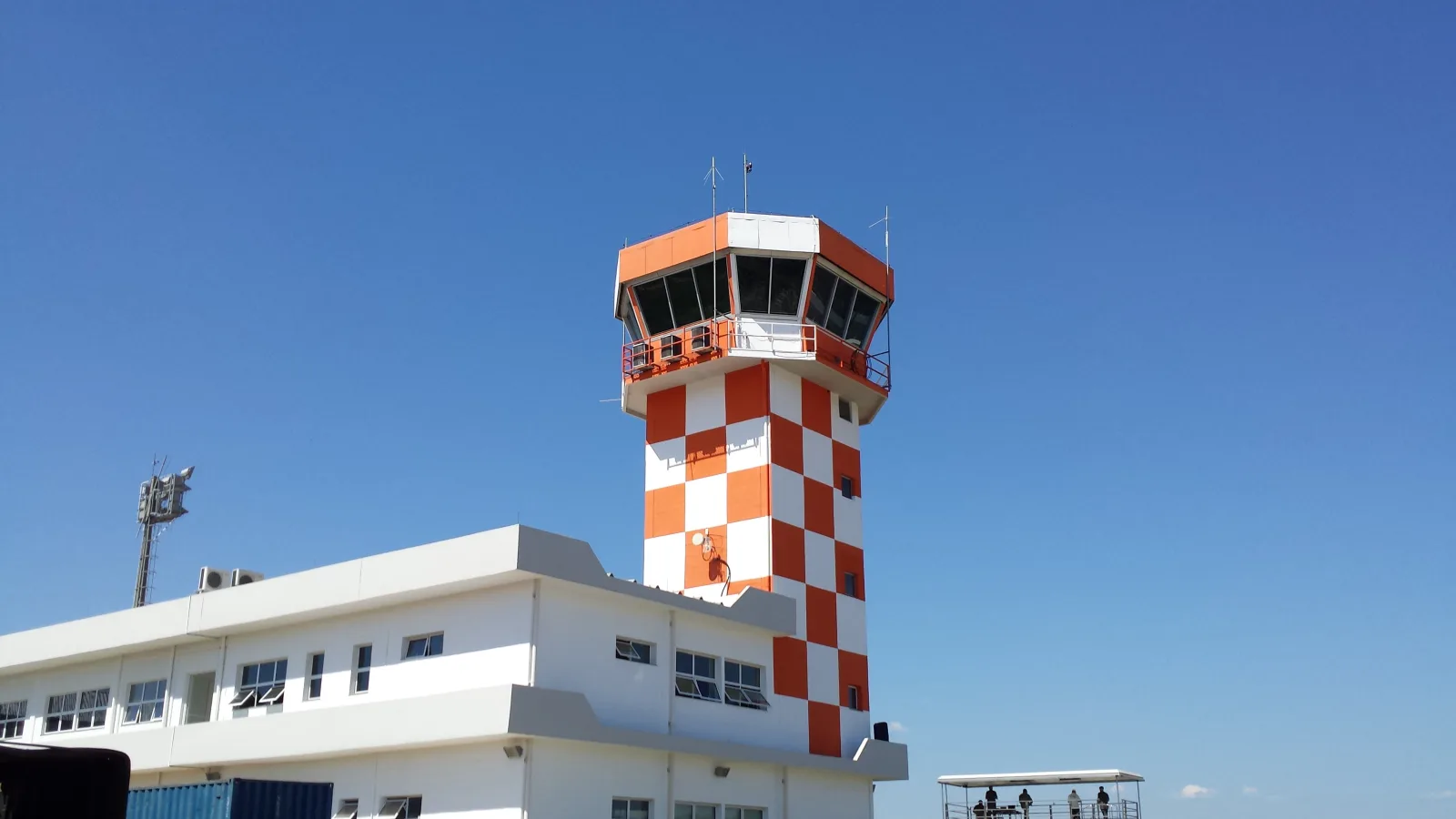 Torre de controle quadriculada de laranja e branco da Base de Aviação de Taubaté, sobre um prédio branco, com céu azul